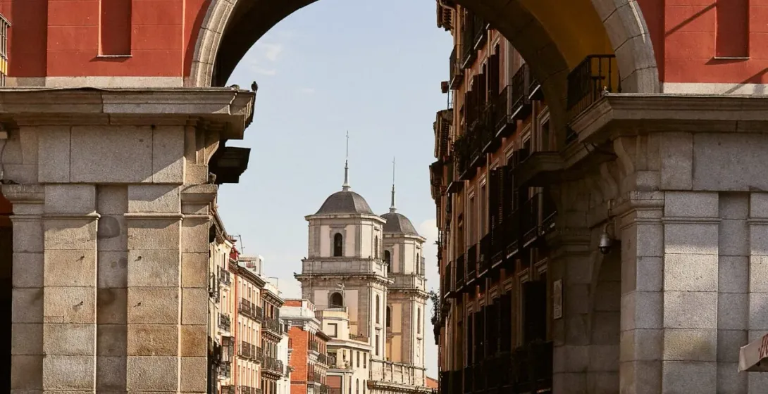 A picturesque archway in Madrid reveals a charming street scene with artists and historic buildings.