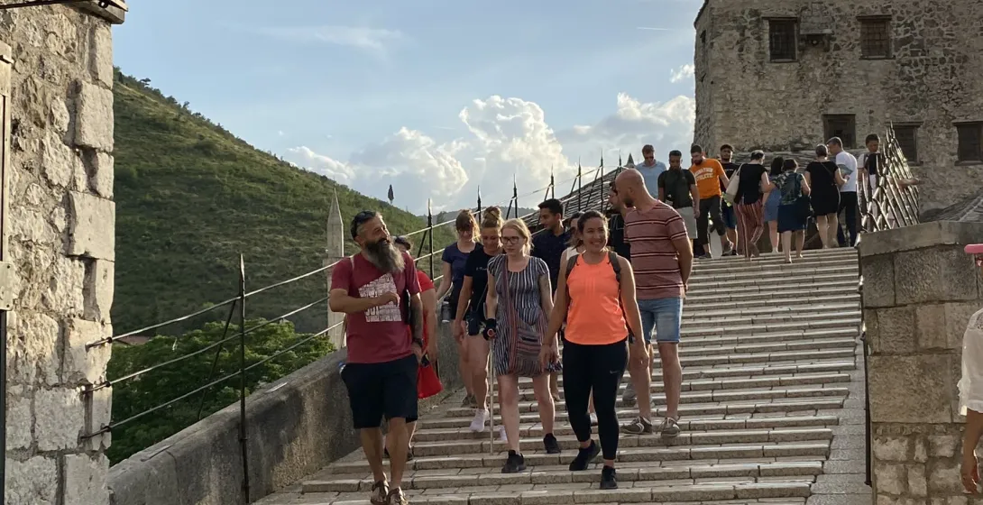 Grupa turystów na wycieczce pieszo po historycznym moście Stari Most w Mostarze.