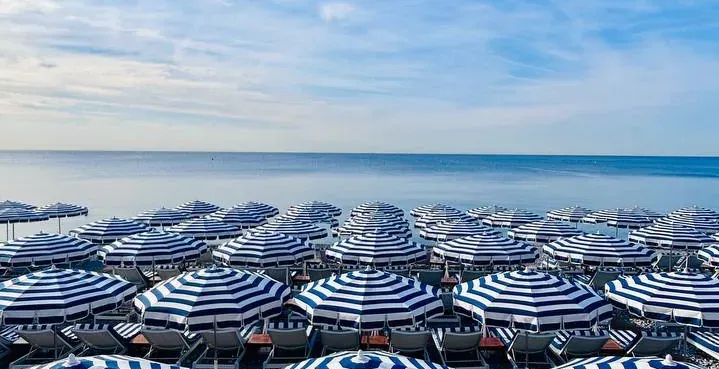 Rzędy niebiesko-białych, pasiastych parasoli i leżaków na plaży w Nicei.