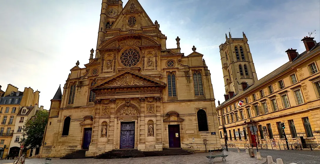 The ornate facade of Saint-Étienne-du-Mont church in Paris, with a clock tower and stained-glass windows, under a partly c...