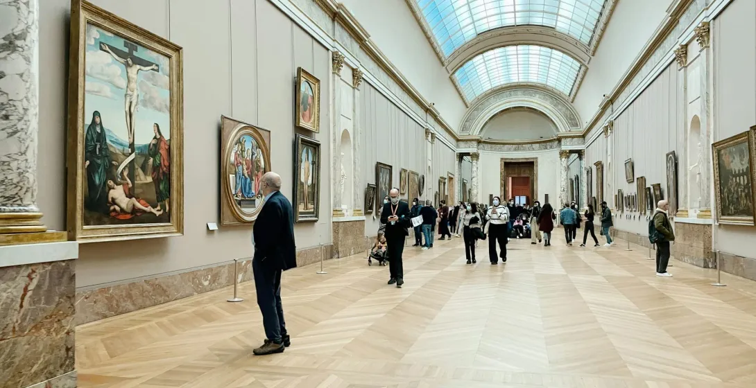 Tourists exploring a grand museum hall filled with art.