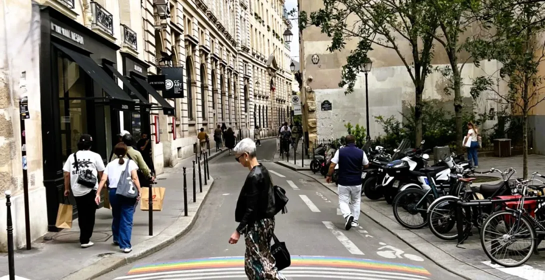 Ein Fußgänger überquert einen Regenbogen-Zebrastreifen in einer charmanten Pariser Straße.