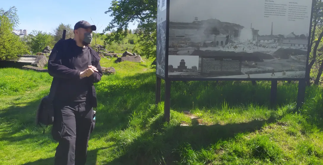Ein Tourist erkundet eine historische Stätte in Polen und liest eine Informationstafel mit historischen Fotos.