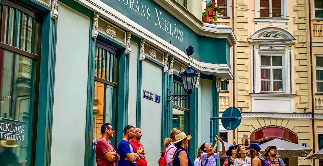 Un grupo de turistas explora las encantadoras calles de Riga, Letonia, haciendo una pausa frente a un restaurante histórico.