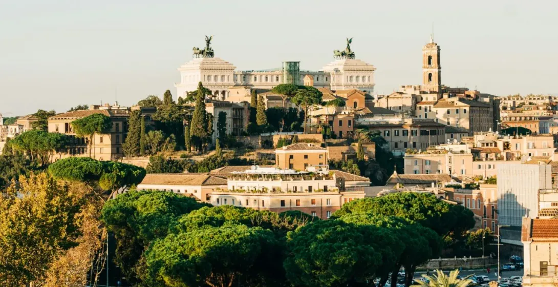 Panoramiczny widok na Rzym z Pomnikiem Wiktora Emanuela II na wzgórzu, ruchliwą ulicą z samochodami i autobusami oraz zielony