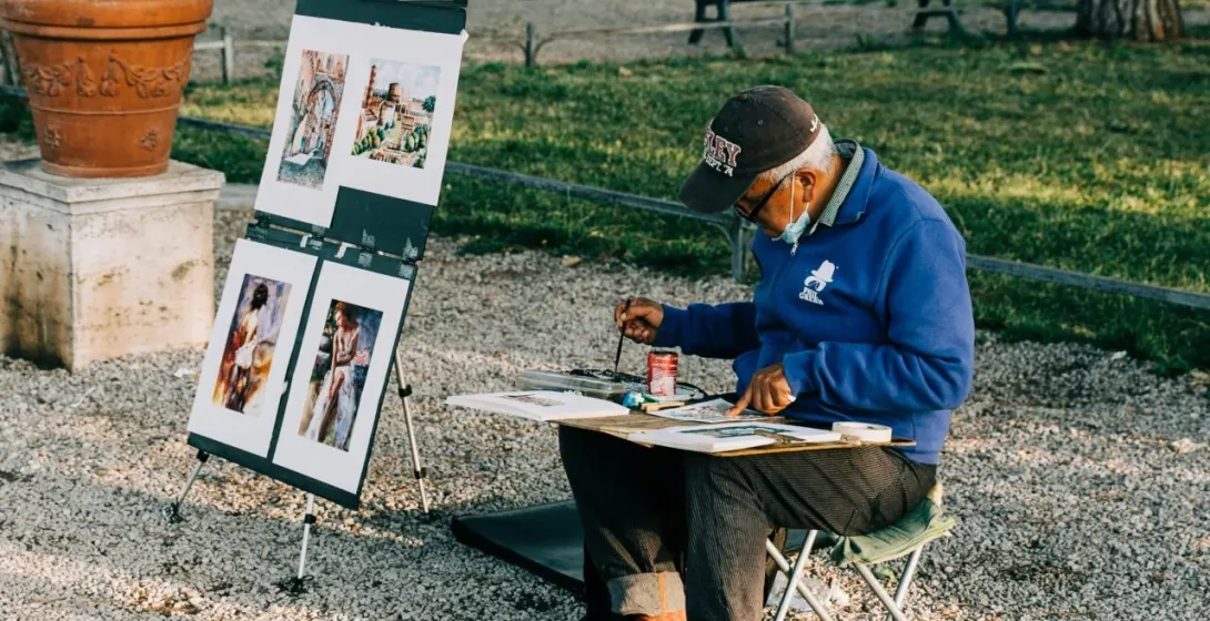 Artista callejero pintando en un parque romano, mostrando obras de arte que representan monumentos famosos.