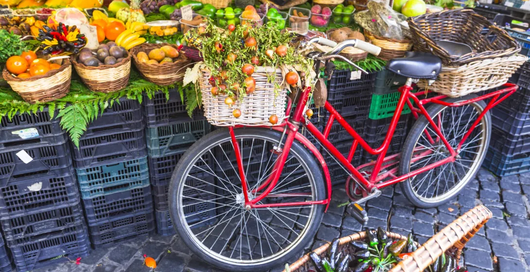Bicicleta roja con fruta en una cesta en un vibrante mercado romano.