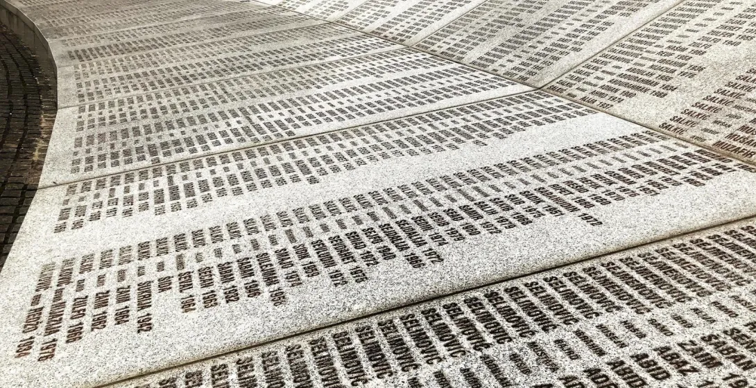 Eine geschwungene Gedenkmauer mit zahlreichen Namen und Daten.