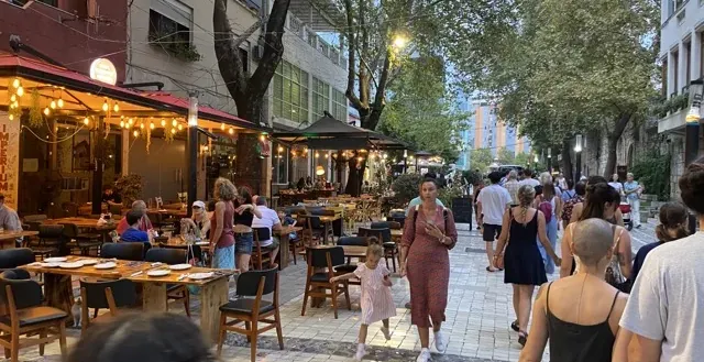 Tętniąca życiem ulica miejska w nocy z restauracjami na świeżym powietrzu i pieszymi.