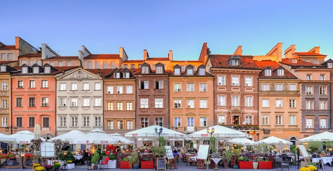 Warszawski Rynek Starego Miasta o zachodzie słońca, z kolorowymi budynkami i urokliwą kawiarnią na świeżym powietrzu.