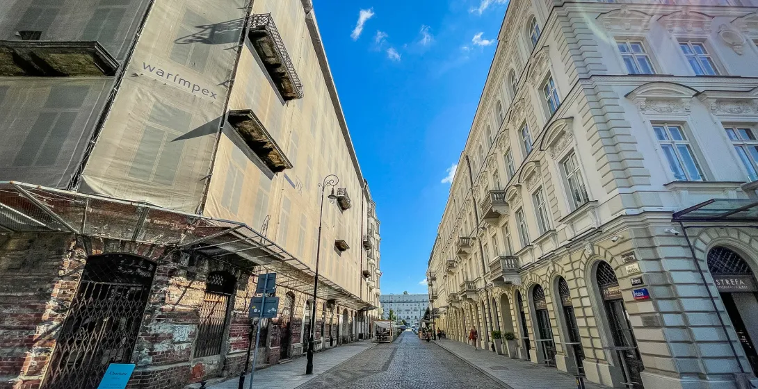 Słoneczna brukowana ulica w Warszawie, z zabytkowymi budynkami i jednym w trakcie remontu.