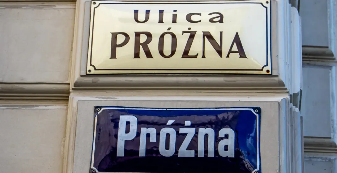 Cztery znaki uliczne na budynku w Warszawie, wszystkie wskazujące ulicę Próżną.