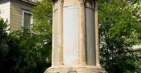 The Choragic Monument of Lysicrates, an ancient monument with Corinthian columns, surrounded by trees and buildings in Ath...
