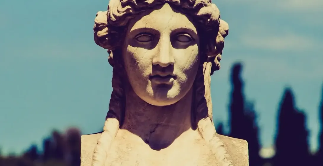 Nahaufnahme einer antiken griechischen Marmorbüste einer Frau mit geflochtenem Haar, vor klarem blauem Himmel.