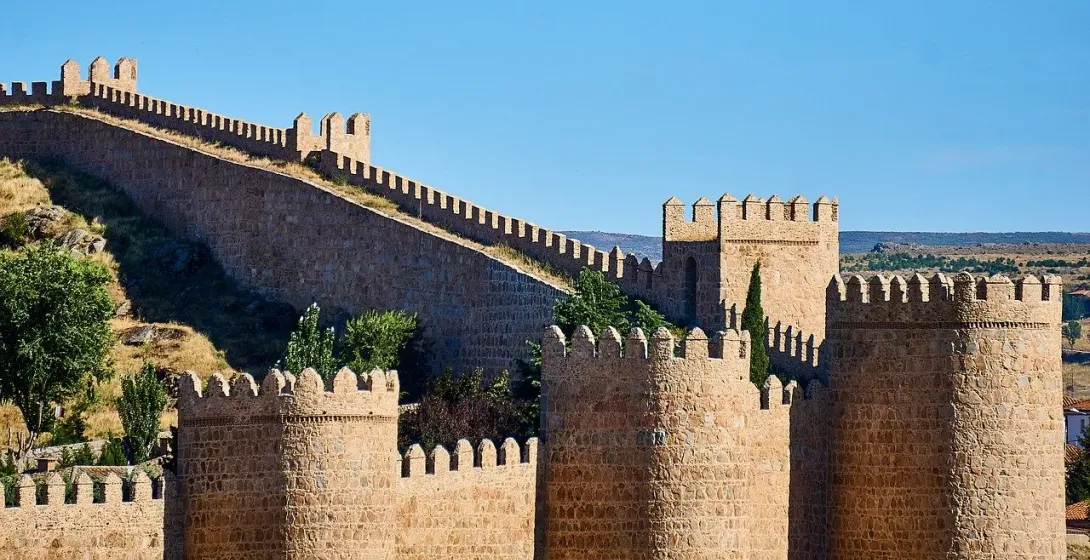 Las murallas medievales de piedra de Ávila, con sus almenas y torres, en un día soleado con un cielo azul y despejado.