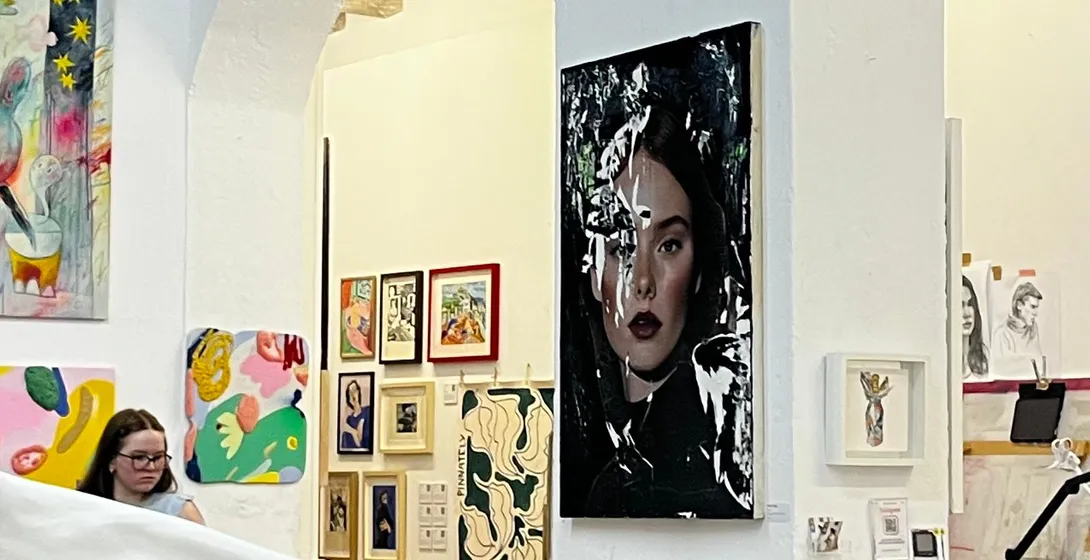 Wnętrze pracowni artystycznej z obrazami na białych ścianach, drewnianymi belkami, białą rzeźbą i kobietą obserwującą sztukę.