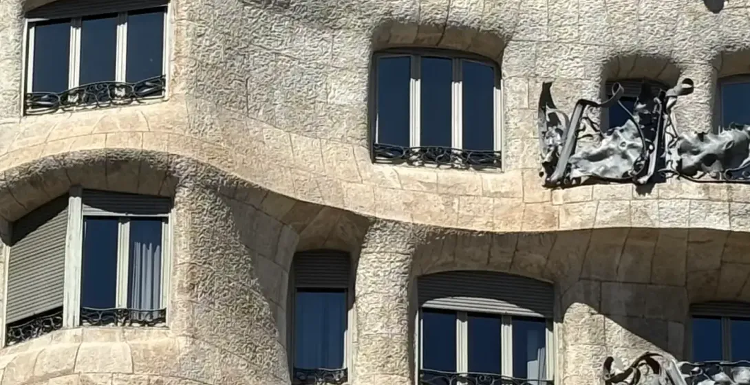 Detalle de la fachada ondulada de piedra de la Casa Milà con ventanas oscuras, persianas grises y balcones de hierro forjado.