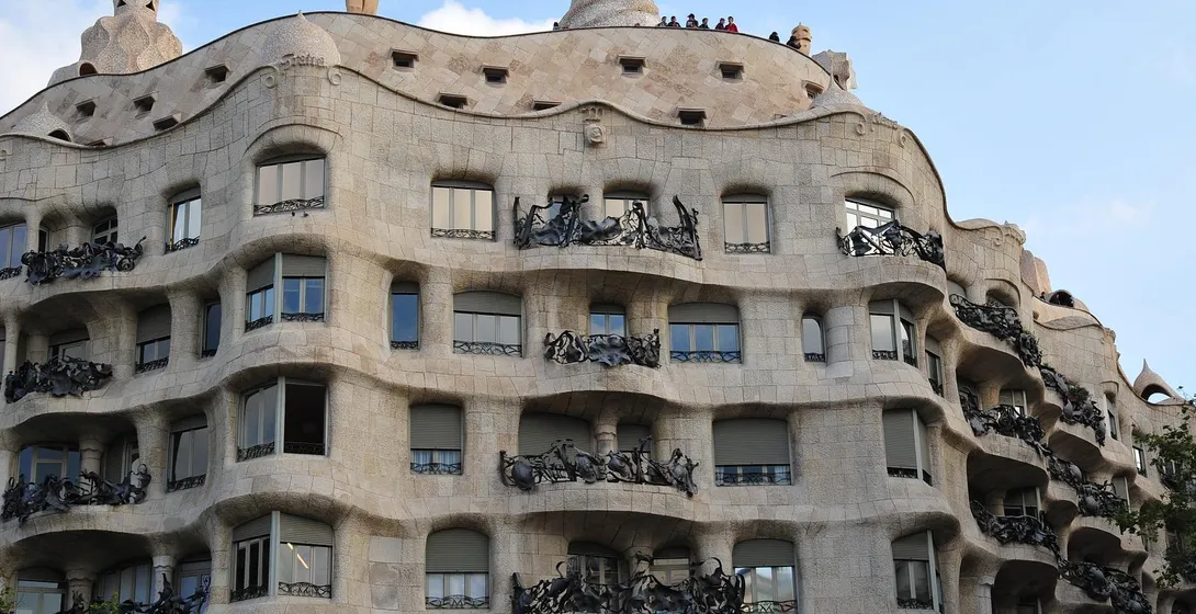 Fachada de piedra curvada de Casa Milà (La Pedrera) con balcones de hierro ornamentados bajo cielo azul, diseñada por Gaudí.
