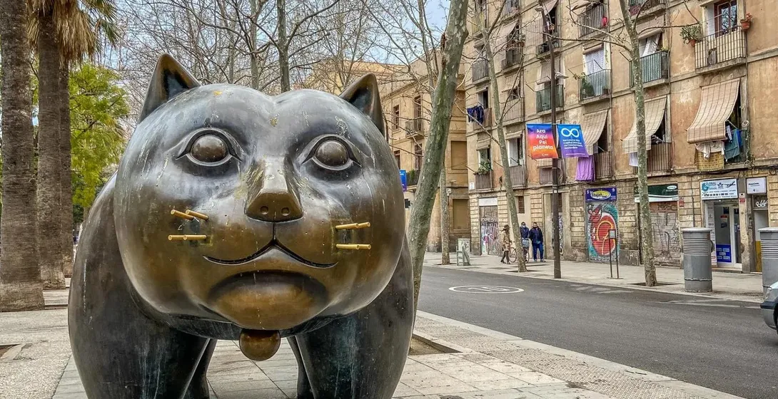 Large bronze cat sculpture by Botero on a sidewalk in Barcelona, with buildings and palm trees in the background.