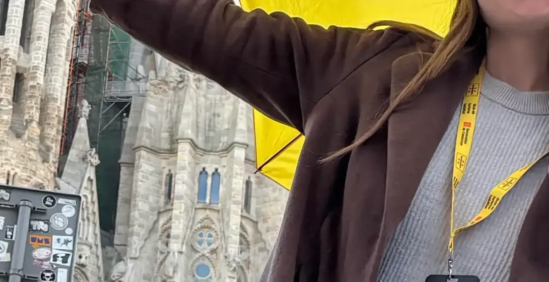 A smiling Walkative guide with a yellow umbrella in front of the Sagrada Familia in Barcelona, with its towers under construc