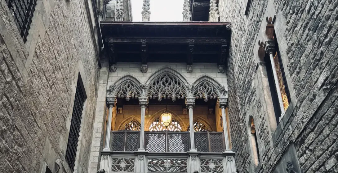 Ornate neo-Gothic stone bridge connecting two buildings over a narrow alleyway in Barcelona's Gothic Quarter.
