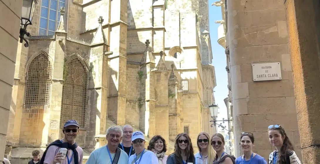 A smiling tour group poses in a narrow street behind the Cathedral of Barcelona in the Gothic Quarter.