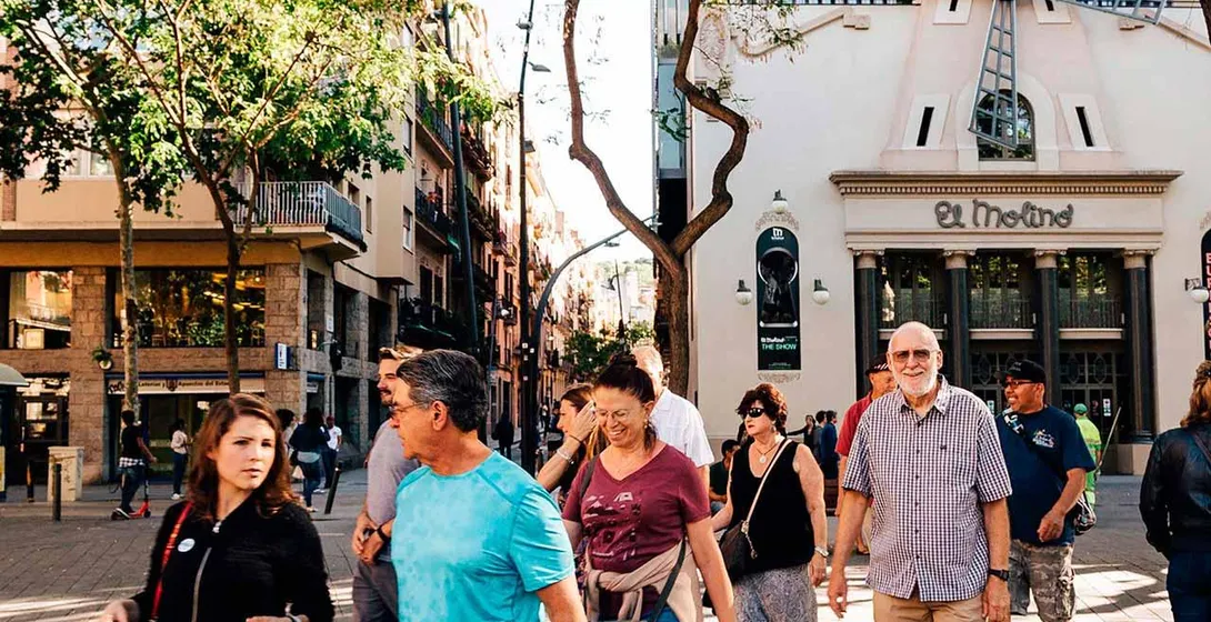 A group of diverse people walking on a sunny city street, passing El Molino theater in Barcelona.