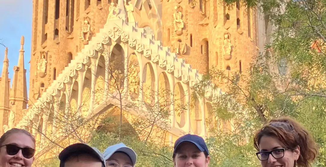 Un grupo diverso de personas sonriendo frente a la ornamentada, parcialmente construida basílica de la Sagrada Familia con...