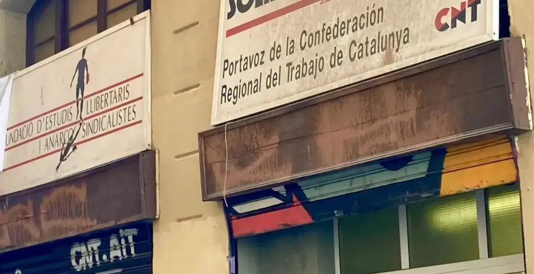 Un grupo de personas en un tour urbano mirando hacia un edificio con letreros de "Solidaridad Obrera" y "CNT" y grafitis.