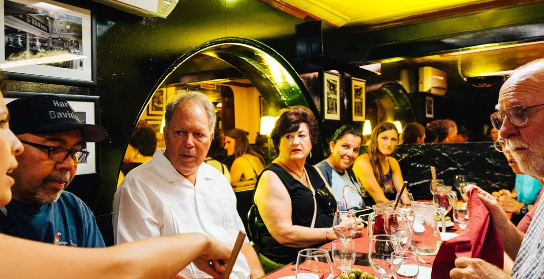 Eine Gruppe von Personen sitzt an einem Restauranttisch mit roten Tischdecken, teilt Tapas, Oliven und einen Krug Sangria.