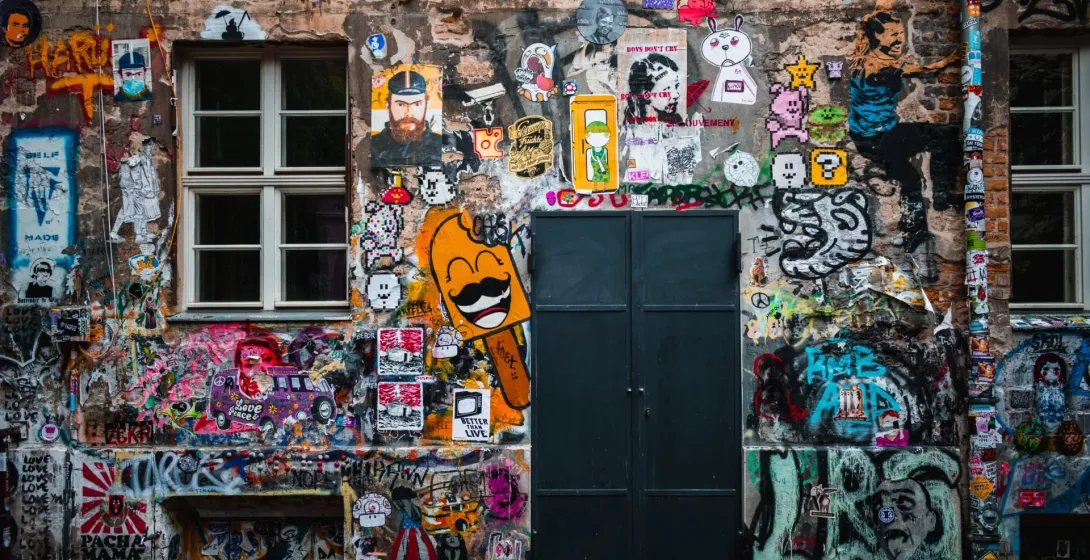 A weathered brick building facade in Berlin, densely covered with colorful street art, graffiti, and stickers.