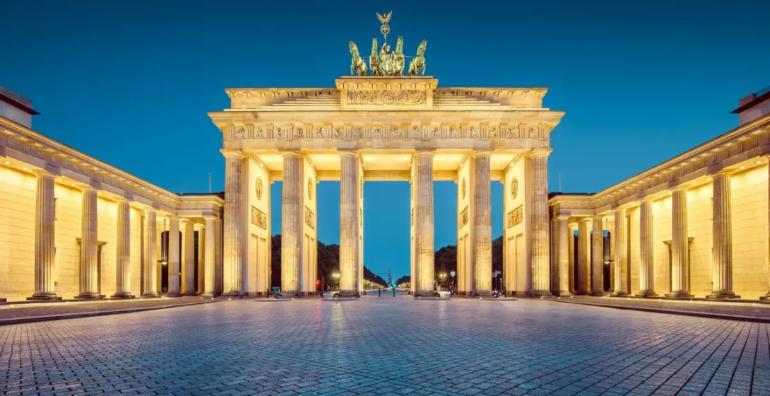 La Puerta de Brandenburgo en Berlín, iluminada al anochecer, con la escultura de la Cuadriga y una amplia plaza empedrada ...