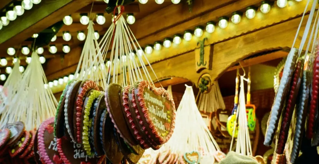 Hängende Lebkuchenherzen mit Zuckergussdekorationen und verschiedenen Süßigkeiten an einem festlichen Marktstand, mit Besu...
