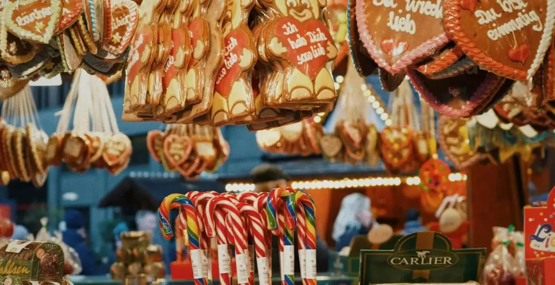 Ein Stand auf einem Weihnachtsmarkt, der Lebkuchenherzen, Zuckerstangen und geröstete Nüsse verkauft.
