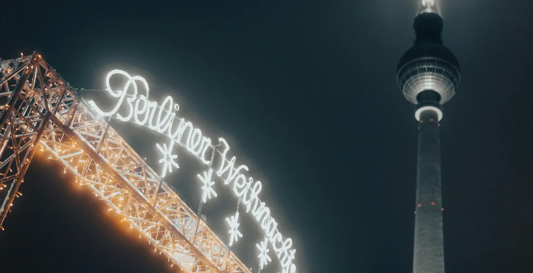 Beleuchtetes Schild 'Berliner Weihnachtszeit' und ein Teil des Berliner Fernsehturms vor dunklem Nachthimmel.