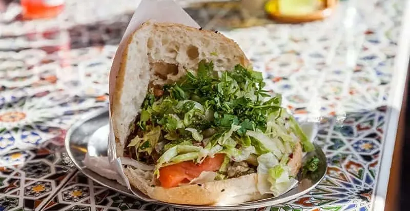 Halber Döner Kebab im Fladenbrot mit Fleisch, Salat, Petersilie und Tomate, auf einem Metallteller auf einem gekachelten T...