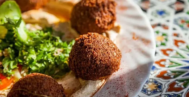 Nahaufnahme eines Tellers mit mehreren goldbraunen Falafelbällchen, Hummus und grünem Petersiliensalat.