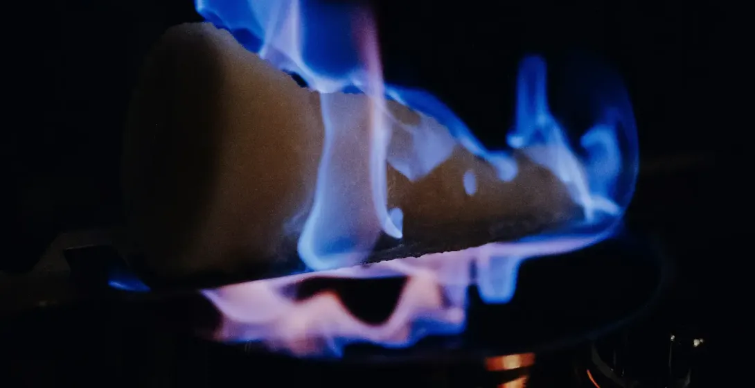 Zuckerhut mit blauen Flammen brennt über einem dunklen Topf, der den Vordergrund vor einem dunklen Hintergrund beleuchtet.