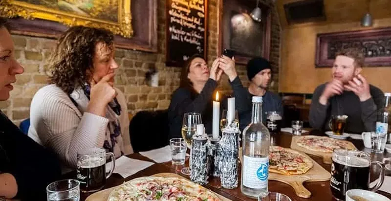 Eine Gruppe von Leuten sitzt an einem langen Tisch in einem gemütlichen Berliner Restaurant, mit Flammkuchen und Getränken.