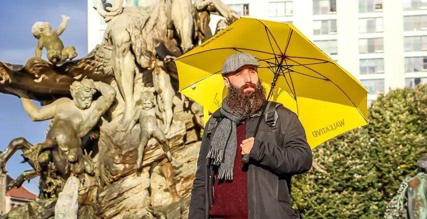 Hombre barbudo con gorra y paraguas amarillo de Walkative, de pie frente a la Fuente de Neptuno en Berlín.
