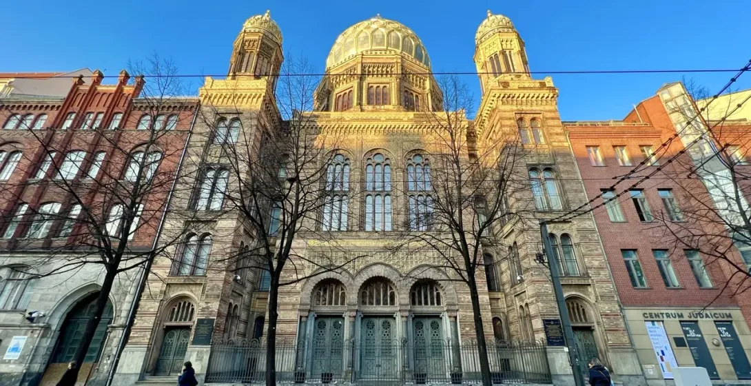 La fachada ornamentada de la Nueva Sinagoga de Berlín en un día soleado, vista desde el otro lado de la calle entre árboles.