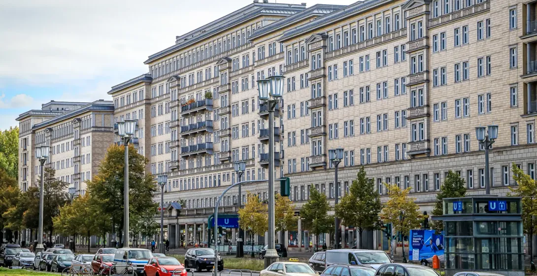 Large multi-story apartment buildings with streetlights, parked cars, trees, and a U-Bahn station entrance in Berlin.