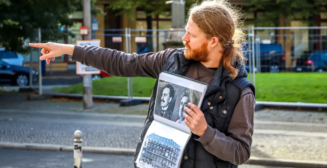 A tour guide in Berlin points while holding a binder with old black-and-white historical photographs.