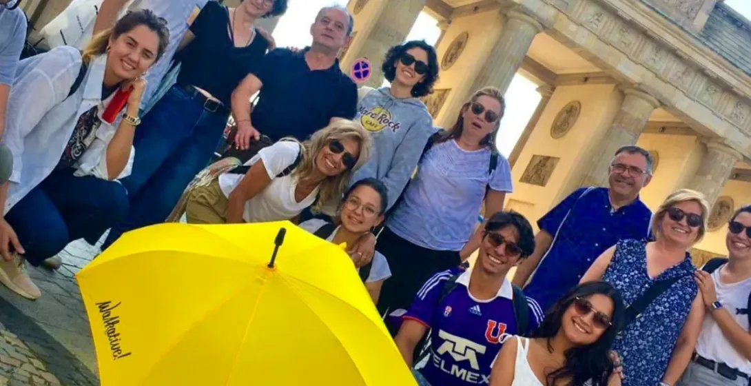 Un grupo diverso de personas posa con un paraguas amarillo de Walkative frente a la Puerta de Brandenburgo en Berlín.