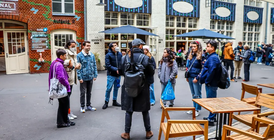 A tour guide with a backpack speaks to a group of people in the Hackesche Höfe courtyard in Berlin.