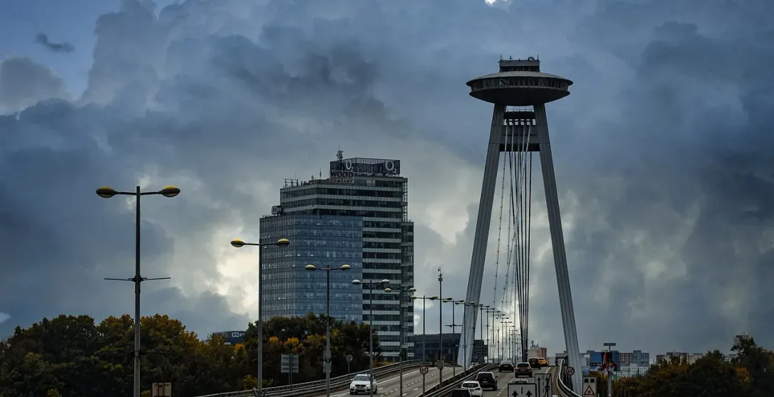 Modern UFO Bridge (Most SNP) in Bratislava with cars on the roadway, a distinctive saucer-shaped restaurant, under dramatic c