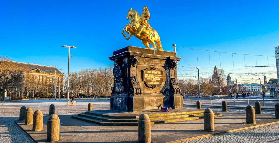Golden equestrian statue of August the Strong on a dark pedestal in a cobblestone square, Dresden.