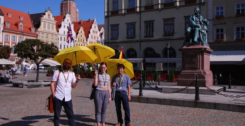 Grupa na pieszej wycieczce po Wrocławiu z żółtymi parasolami.