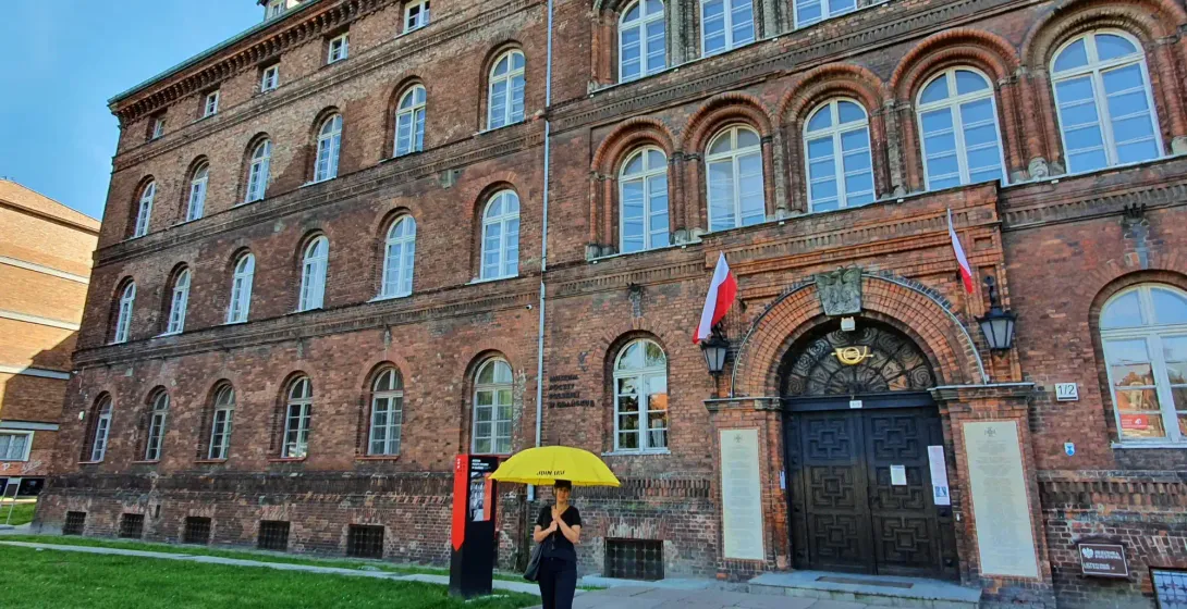 Historic brick building of the Polish Post Office in Gdansk with arched windows, a dark entrance, and Polish flags. A pers...