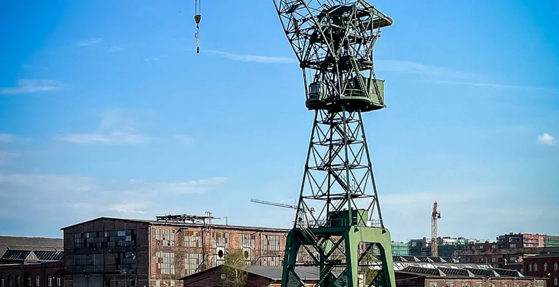 Large green gantry crane standing over the Motława River, with historic shipyard buildings under a clear blue sky in Gdańsk.